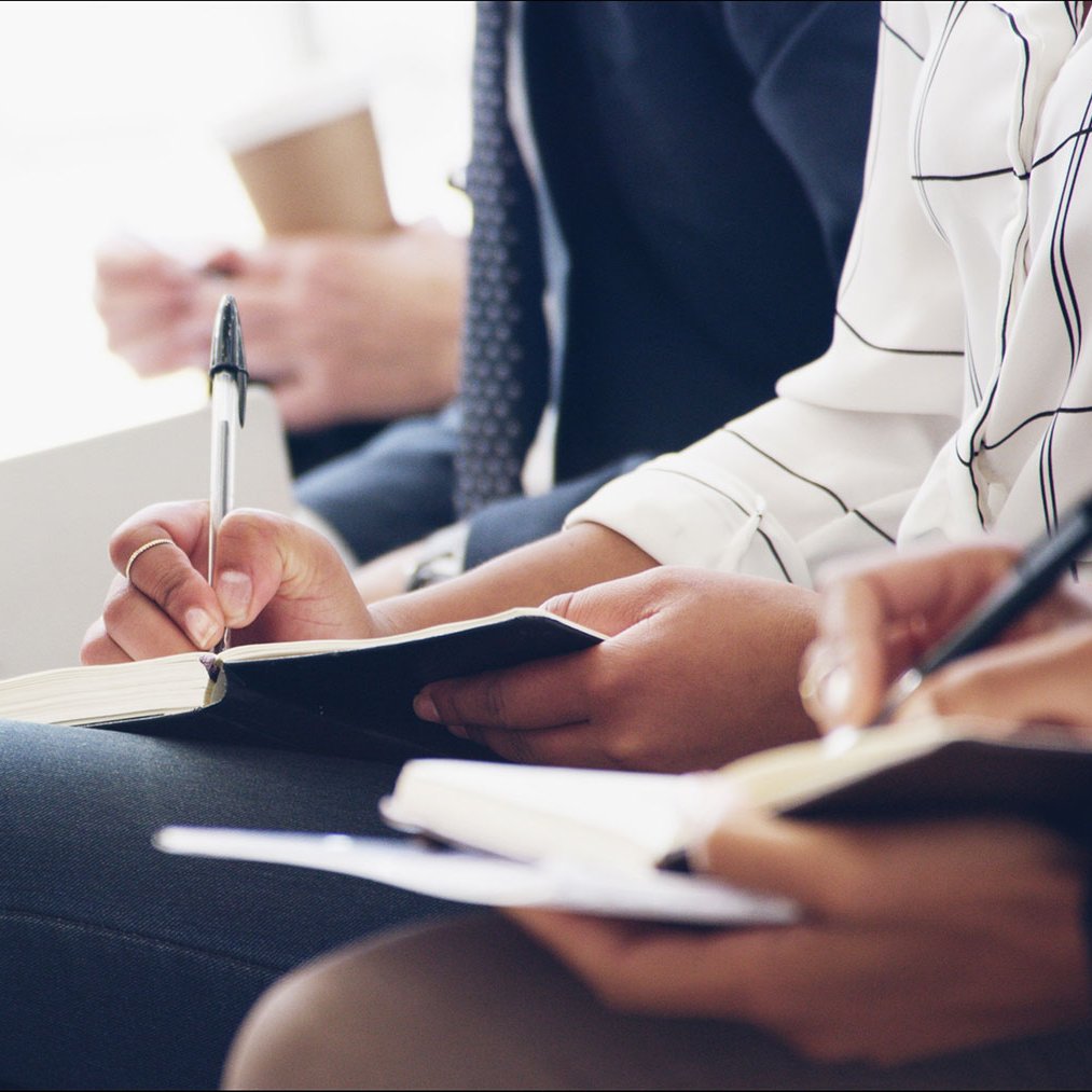 Mehrere Personen sitzen nebeneinander und schreiben in Notizbücher