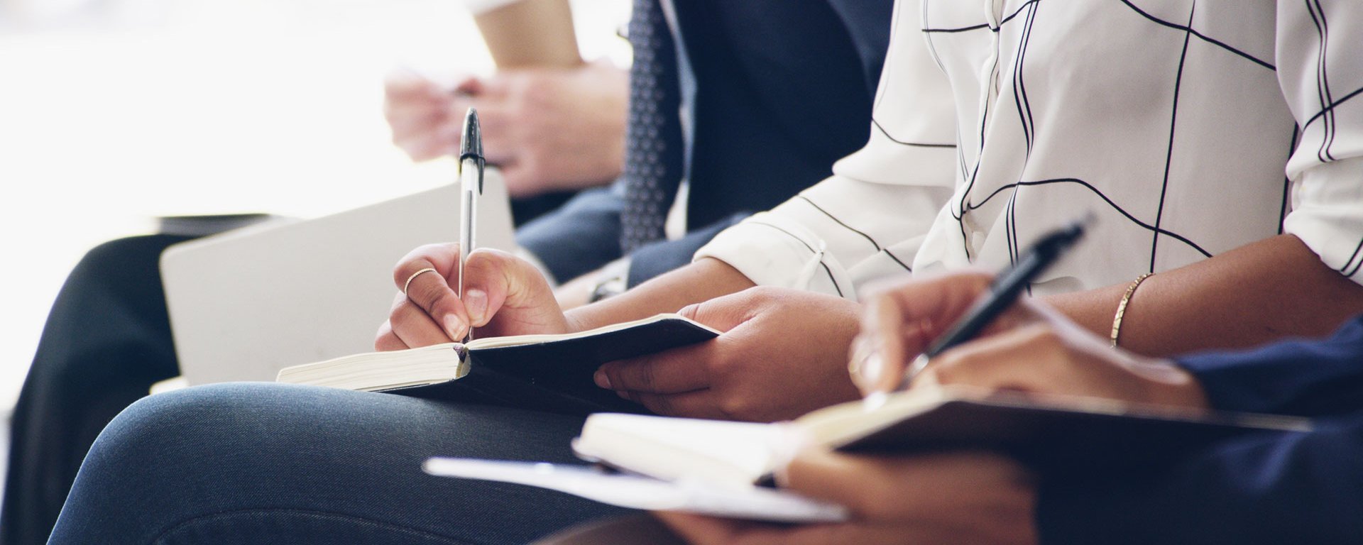 Mehrere Personen sitzen nebeneinander und schreiben in Notizbücher