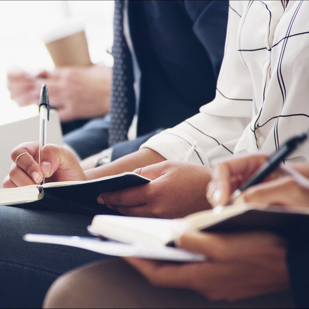 Mehrere Personen sitzen nebeneinander und schreiben in Notizbücher