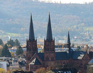 Die Kirche Sankt Johann, Johanneskirche, in Freiburg überragt die Dächer der Gebäude im Umfeld. Bäume sind herbstlich gefärbt.